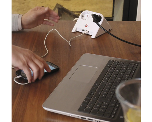 Steckdosenadapter mit USB Anschlüssen auf einem Tisch mit Laptop und Handy