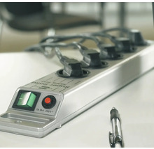 Mehrfachsteckdose mit fünf Steckplätzen und angeschlossenen Stromkabeln auf einem Tisch