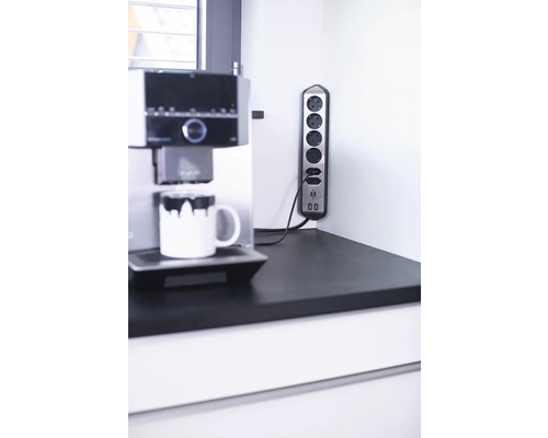 Steckdosenleiste mit fünf Steckdosen und zwei USB-Anschlüssen neben einer Kaffeemaschine auf einer Arbeitsplatte