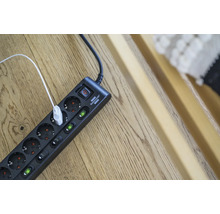 Mehrfachsteckdose mit Schalter und eingestecktem USB-Kabel auf einem Holzboden
