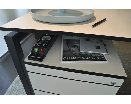 Detailansicht eines Schreibtisches mit Mehrfachsteckdose, Zeitschriften und einem Stift