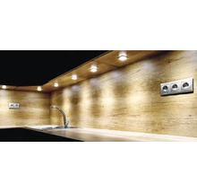 Moderne Küche mit Rückwand in Holzoptik, LED-Unterbauleuchten beleuchten eine Arbeitsplatte mit Spülbecken und verchromter Armatur.
