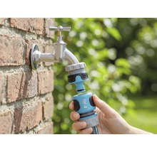 Gartenszene mit Wasserhahn, daran angeschlossen ein for_q Gartenschlauch-Kupplungsstück in der Hand
