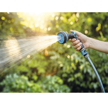Hand hält Gartenschlauch mit Sprühkopf beim Bewässern
