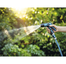Eine Person hält eine Gartenspritze und bewässert Pflanzen.