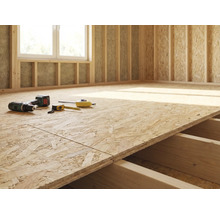 Rohbau eines Zimmers mit OSB-Plattenboden, Bohrmaschine und Messwerkzeugen.