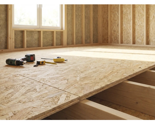 Rohbau eines Zimmers mit OSB-Plattenboden, Bohrmaschine und Messwerkzeugen.