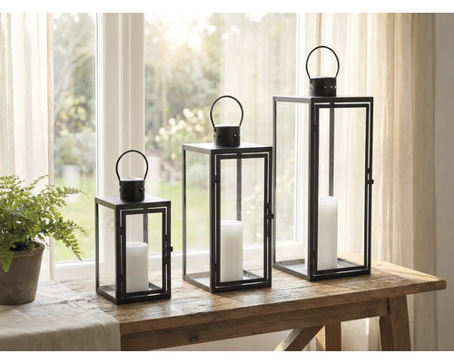 Drei dekorative Windlichter aus Metall und Glas mit Kerzen auf einem Tisch.