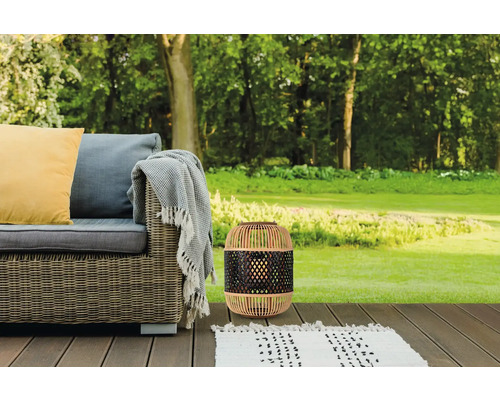 Gartenszene mit Rattan-Laterne, Outdoor-Sofa und Teppich auf einer Holzterrasse