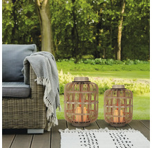 Gartenszene mit Rattansessel, Decke, Teppich und zwei Windlichtern aus Rattan mit LED-Kerzen.