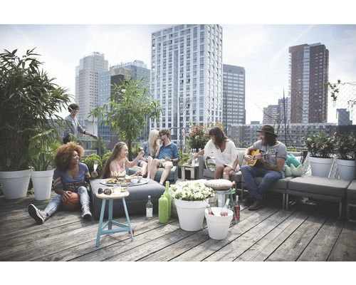 Gruppe von Freunden entspannt sich auf einer Dachterrasse mit Stadtblick, Gartenmöbeln, Pflanzen in Töpfen und Getränken