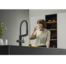 Frau trinkt Wasser aus einem Glas neben einem Wasserhahn in einer Küche