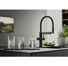 Drei Gläser mit Wasser neben einer schwarzen Küchenarmatur auf einer Küchentheke.