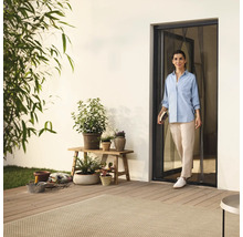 Frau betritt Terrasse durch Insektenschutztür, umgeben von Pflanzen und Gartenzubehör.