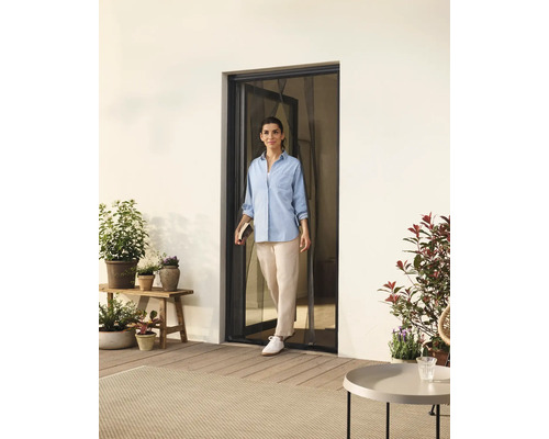 Frau geht durch eine Tür mit Insektenschutzgitter auf eine Terrasse mit Pflanzen