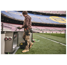 Mann mit Werkzeuggürtel und Arbeitskleidung bei der Arbeit an einem Schaltschrank im Stadion.