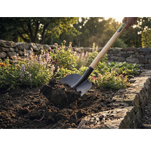 Eine Schaufel hebt Erde in einem Gartenbeet an.