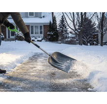 Person schaufelt Schnee mit einer Schneeschaufel von einem Gehweg