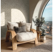 Hell eingerichteter Wohnbereich mit Holz-Sessel, Teddy-Polstern, botanischer Mustertapete, Zimmerpflanzen und großem Bogenfenster mit Stadtblick.