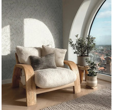 Einladender Wohnbereich mit Holzsessel, flauschigen Kissen, Vliestapete mit Blattmuster und großem Rundbogenfenster mit Blick über die Stadt.