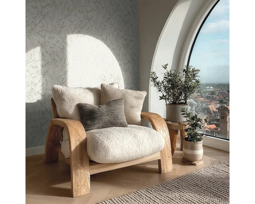 Einladender Wohnbereich mit Holzsessel, flauschigen Kissen, Vliestapete mit Blattmuster und großem Rundbogenfenster mit Blick über die Stadt.