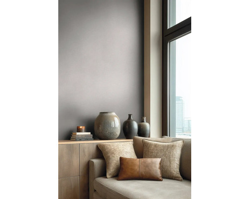 Modernes Wohnzimmer mit graubrauner Tapete, Sofa mit Dekokissen und Vasen auf einem Sideboard neben einem großen Fenster.