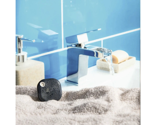 Schwarzer Wassersensor auf einem grauen Handtuch vor einer Waschbeckenarmatur in einem hellen Badezimmer.