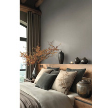 Modernes Schlafzimmer mit Kopfteil aus Holz, grauen Wänden, Zierkissen, Keramikvasen und einem großen Zweig mit Beeren in einer Vase.