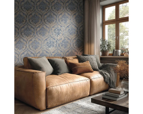 Helles Wohnzimmer mit blau-beiger Damasttapete hinter einem braunen Ledersofa mit Kissen und einem Holzfenster.