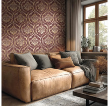 Wohnzimmer mit Tapete im Damast-Muster in Dunkelrot und Gold, braunem Ledersofa mit Kissen und einem Fenster.