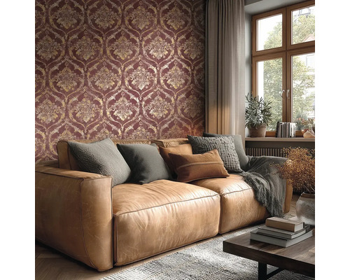 Wohnzimmer mit Tapete im Damast-Muster in Dunkelrot und Gold, braunem Ledersofa mit Kissen und einem Fenster.
