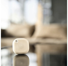 Kleiner quadratischer Bluetooth Smart Home Button mit kreisförmiger Textur und Befestigungsloch auf einer reflektierenden Oberfläche.