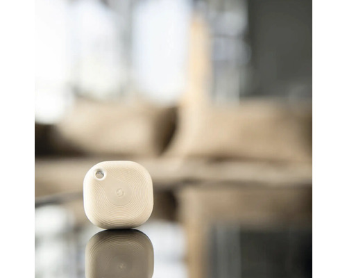 Kleiner quadratischer Bluetooth Smart Home Button mit kreisförmiger Textur und Befestigungsloch auf einer reflektierenden Oberfläche.