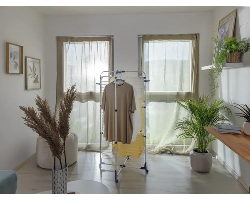 Wohnraum mit Wäscheständer, Kleidung, Fenstern mit Vorhängen und Dekorationen.