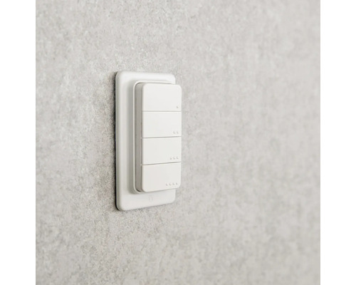 Weißer smarter Wandschalter mit vier Tasten montiert an einer grauen strukturierten Wand.