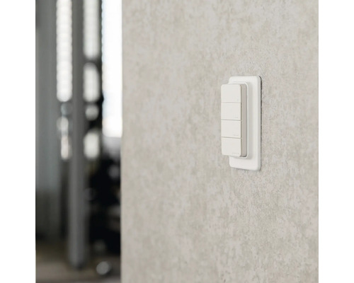 Smarter Wandschalter aus Kunststoff mit vier Tasten zur Lichtsteuerung an einer strukturierten Wand.
