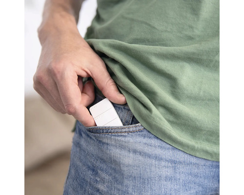 Eine Hand steckt ein kleines weißes Smart-Home-Steuergerät in eine Jeanstasche.