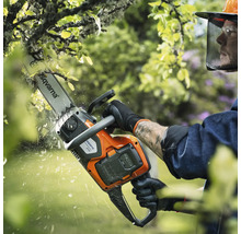 Eine Person benutzt eine Akku-Kettensäge von Husqvarna zum Beschneiden eines Baumes.