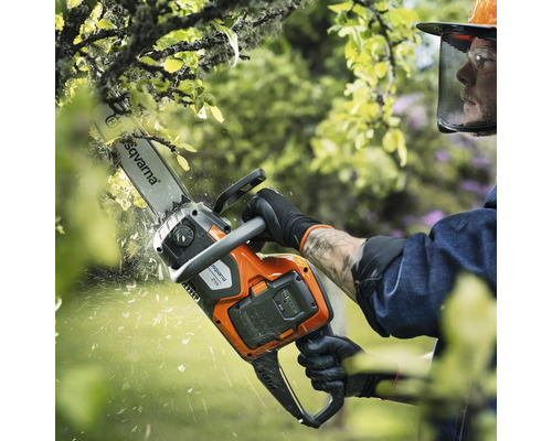 Eine Person benutzt eine Akku-Kettensäge von Husqvarna zum Beschneiden eines Baumes.