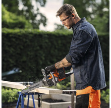 Mann sägt Holz mit einer Husqvarna Kettensäge, die auf einer Werkbank liegt.