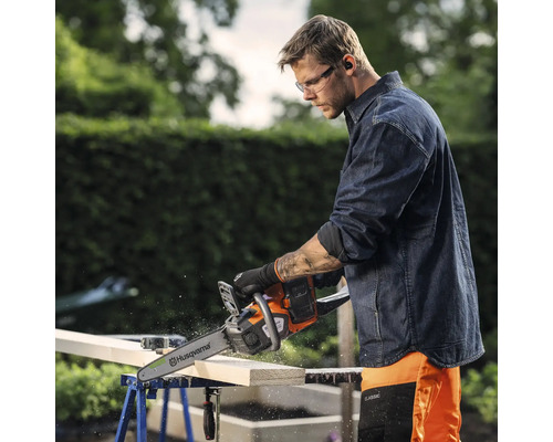 Mann sägt Holz mit einer Husqvarna Kettensäge, die auf einer Werkbank liegt.