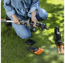 Frau hockt auf Rasen und montiert eine Akku-Heckenschere. Zubehör liegt auf dem Rasen.