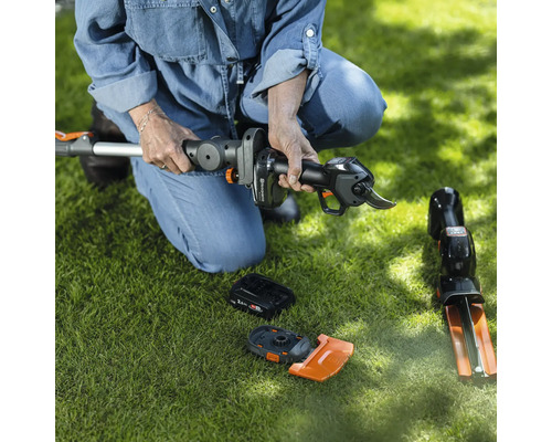 Frau hockt auf Rasen und montiert eine Akku-Heckenschere. Zubehör liegt auf dem Rasen.
