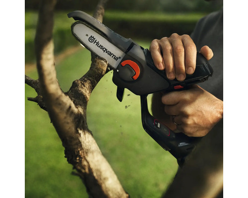 Person bedient Akku-Kettensäge von Husqvarna zum Beschneiden eines Astes.