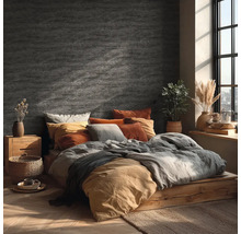 Schlafzimmer mit Wandgestaltung in Steinoptik, Holzbett, Textilien in Erdtönen und hellem Tageslicht durch ein Fenster.