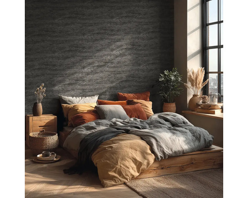 Schlafzimmer mit Wandgestaltung in Steinoptik, Holzbett, Textilien in Erdtönen und hellem Tageslicht durch ein Fenster.
