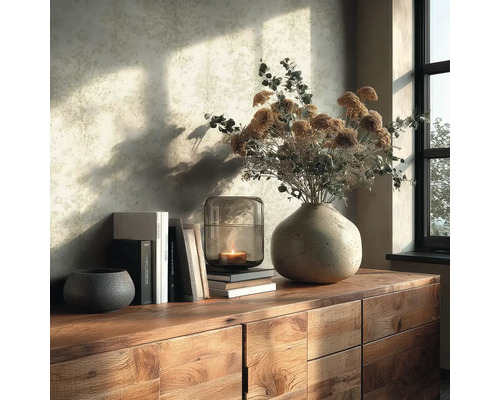 Holzkommode mit Keramikvase, Trockenblumen, Glaswindlicht mit brennender Kerze, Büchern und Dekoschale vor einer hell gemusterten Tapete.