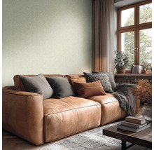 Wohnzimmer mit strukturierter hellgrüner Tapete, braunem Ledersofa mit Kissen, Fenster mit Holzrahmen und einer hellen, wohnlichen Atmosphäre.