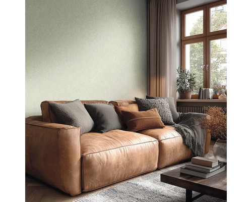 Wohnzimmer mit strukturierter hellgrüner Tapete, braunem Ledersofa mit Kissen, Fenster mit Holzrahmen und einer hellen, wohnlichen Atmosphäre.