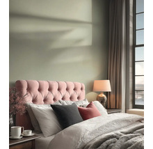 Helles Schlafzimmer mit einem rosa gesteppten Kopfteil, hellgrüner Wandfarbe, gemütlicher Bettwäsche und einer Tischlampe.